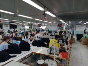 Textile manufacturing factory with workers and sewing machines operating in large scale garment production environment